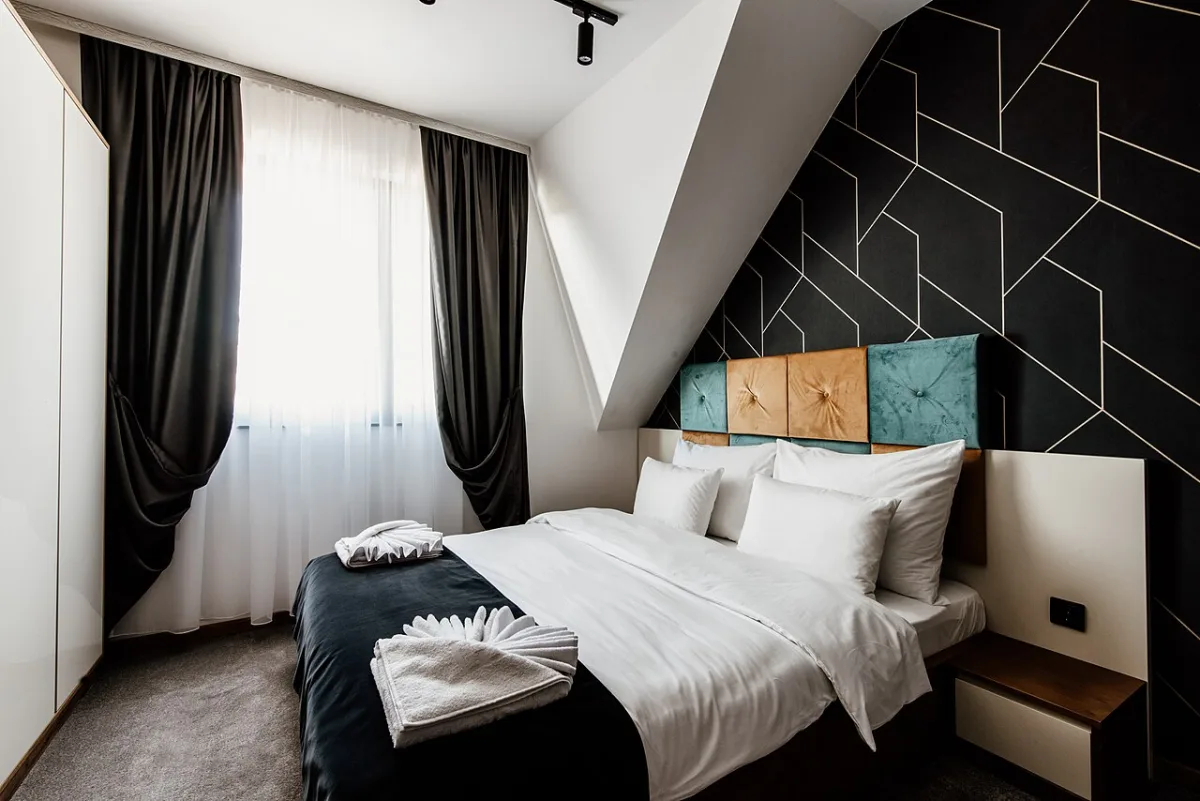 Moderne slaapkamer met een geometrisch wandpatroon in zwart en goud boven het bed met wit beddengoed