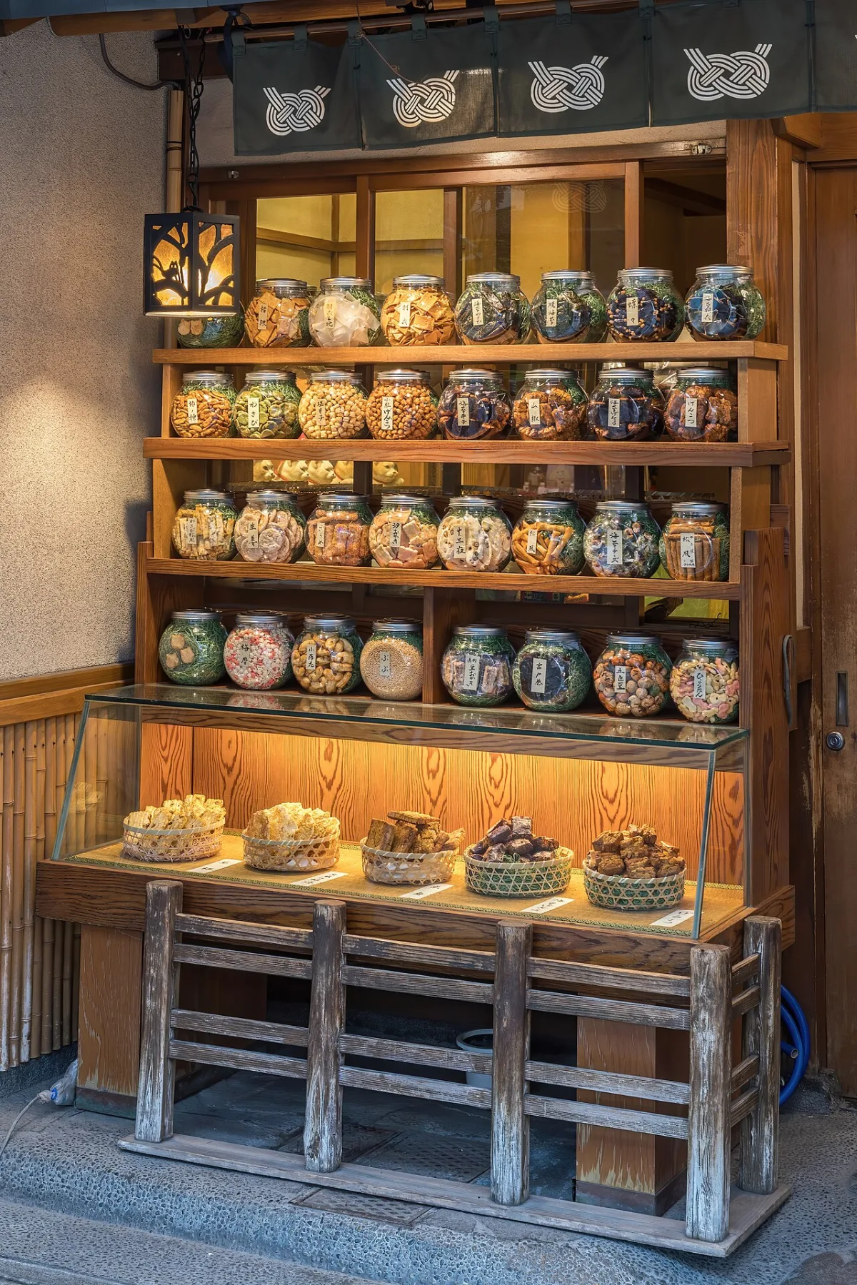 Houten wandplank met verlichte glazen potten vol snacks bij een winkel in Tokio